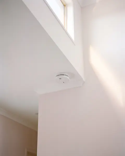 Slim white smoke alarm on a hallway ceiling in soft daylight